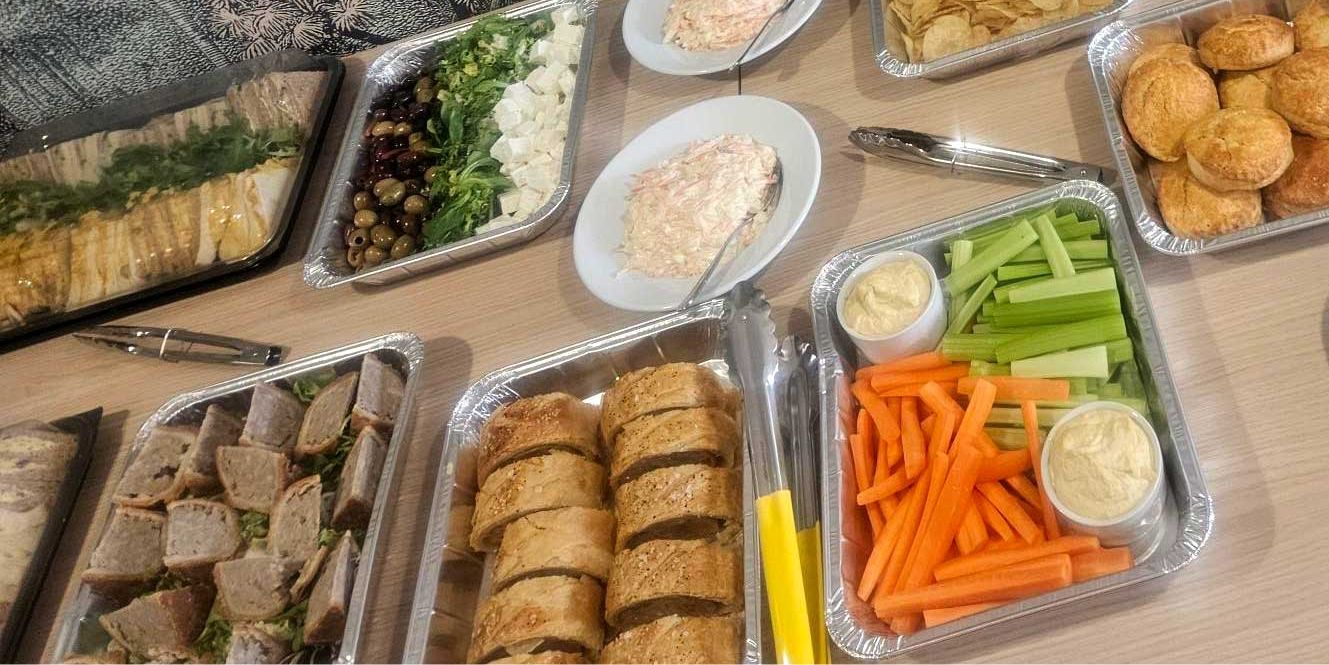 Catering trays of sandwiches, sausage rolls, vegetable sticks with dips, olives and salads, ready for a business buffet.