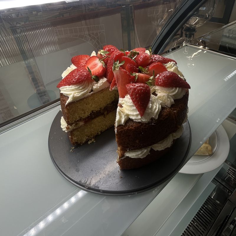A strawberry sponge cake with cream, a slice cut out, in the chilled display.