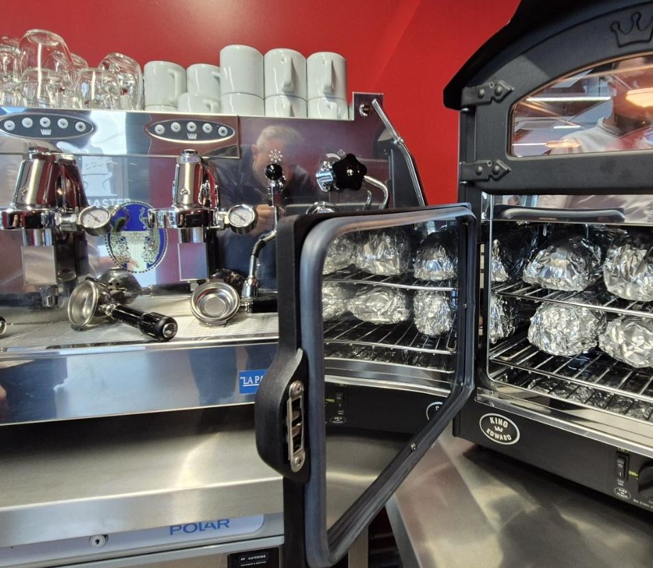 The bistro's espresso machine beside a jacket potato oven, against a red wall.