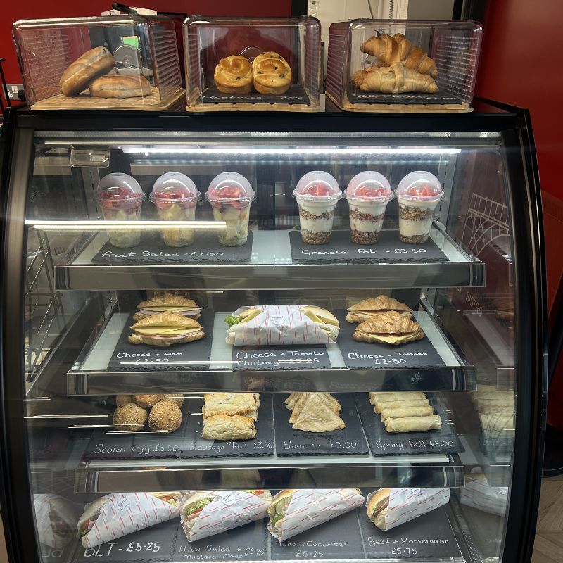 The counter display: pastries on top, fruit pots, sandwiches, savouries and wraps on the shelves below.
