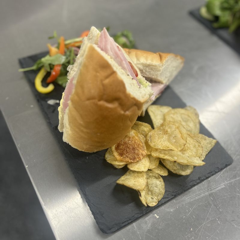 A filled baguette with crisps and salad on a slate.