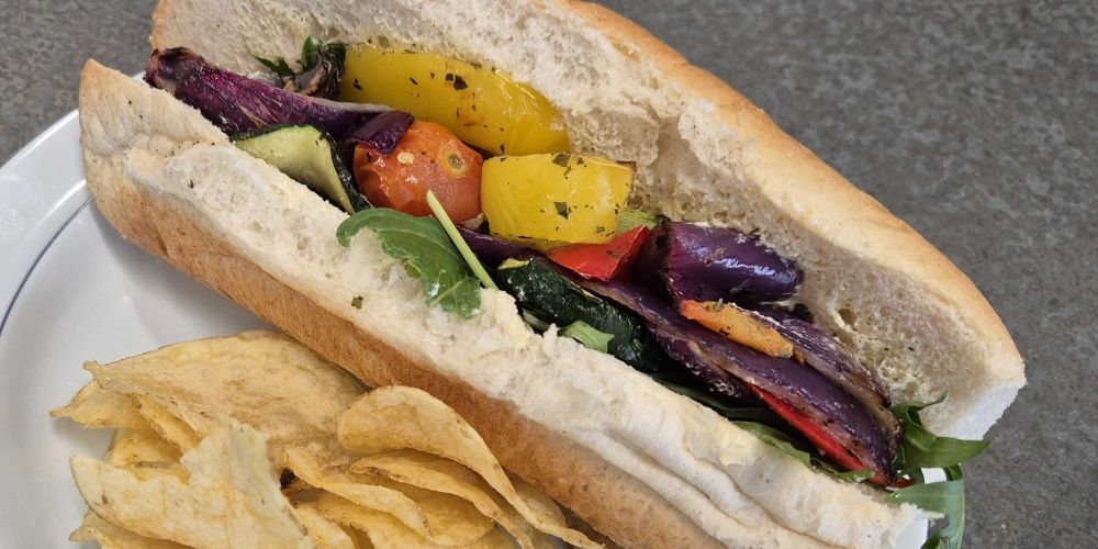 A sub roll filled with roasted peppers, aubergine and spinach, with crisps.